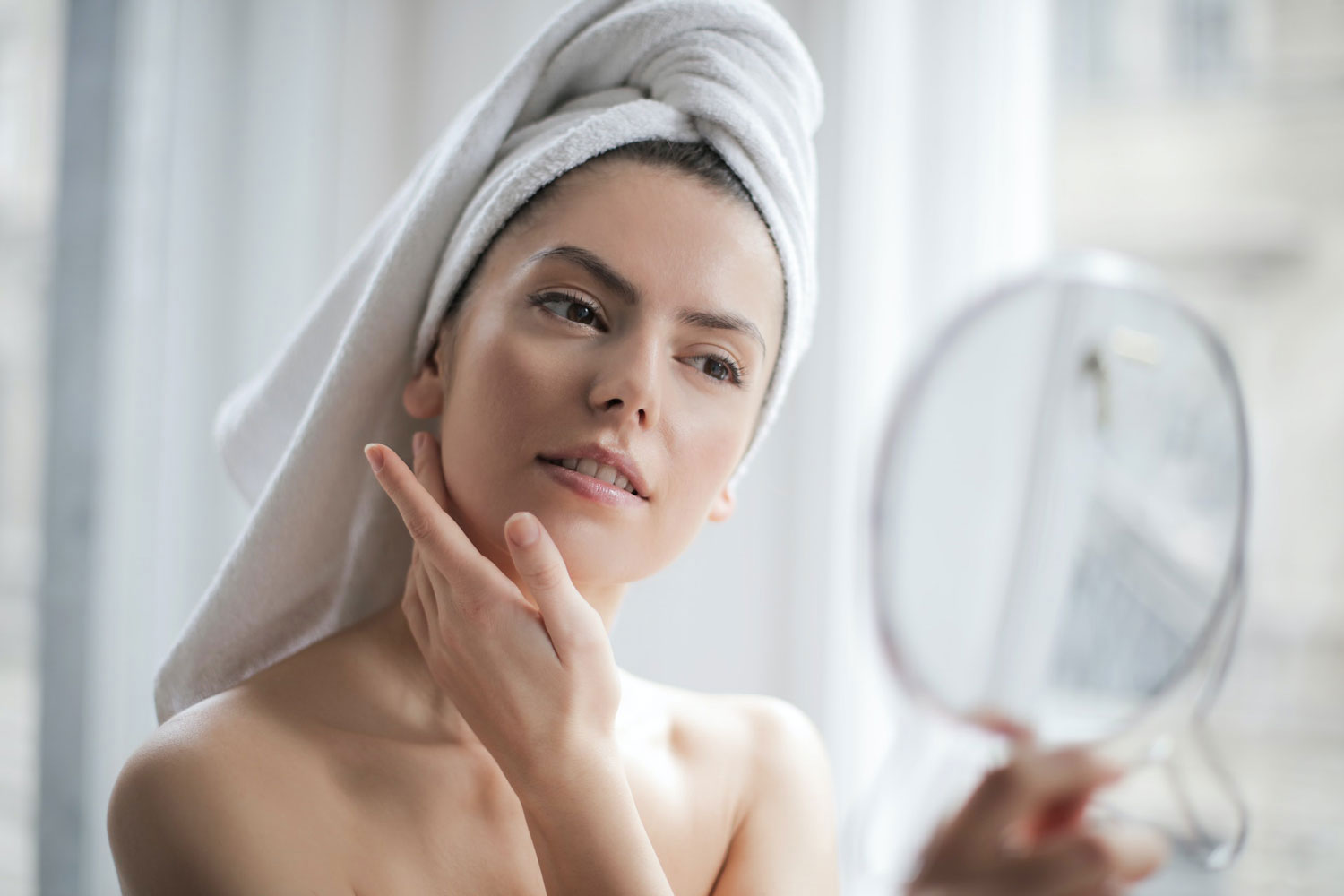 photo of woman admiring her skin while she looks into a mirror she is holding